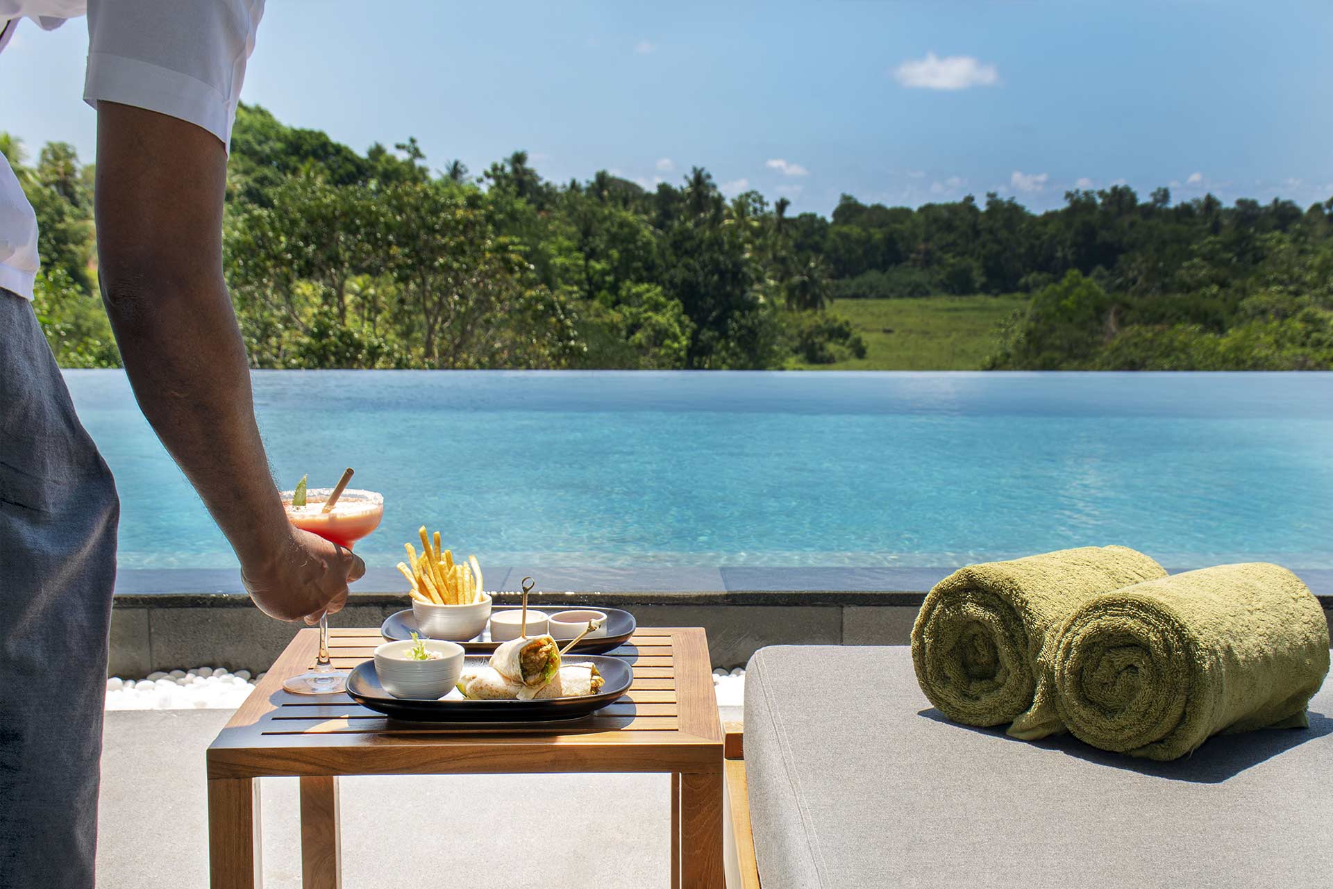 a la carte dishes along with a cocktail being served beside the salt water pool